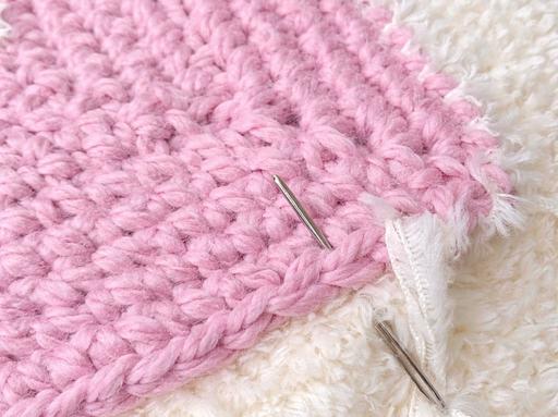 Close-up of a pink textured fabric being stitched to fluffy white material with a silver sewing needle; no text visible. Free crochet pattern