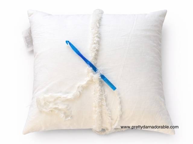 White pillow with a blue crochet hook and white yarn on top; www.prettydarnadorable.com appears in the bottom right corner. Free crochet pattern