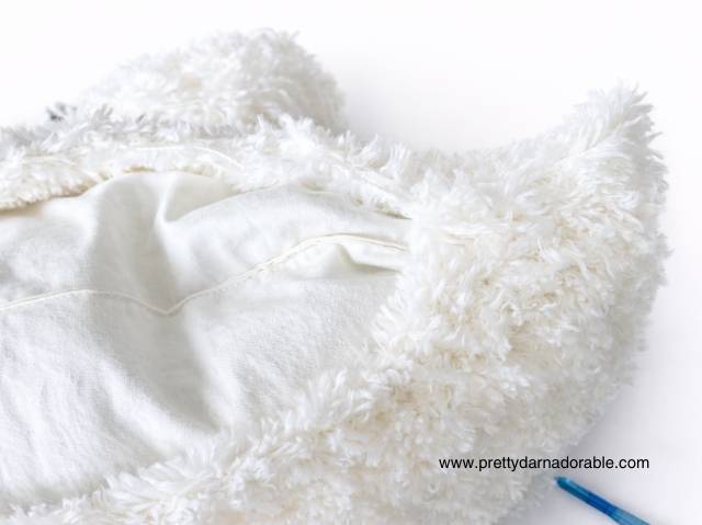 Close-up of a fluffy white fabric piece with an opening showing its soft interior; www.prettydarnadorable.com in corner. Free crochet pattern