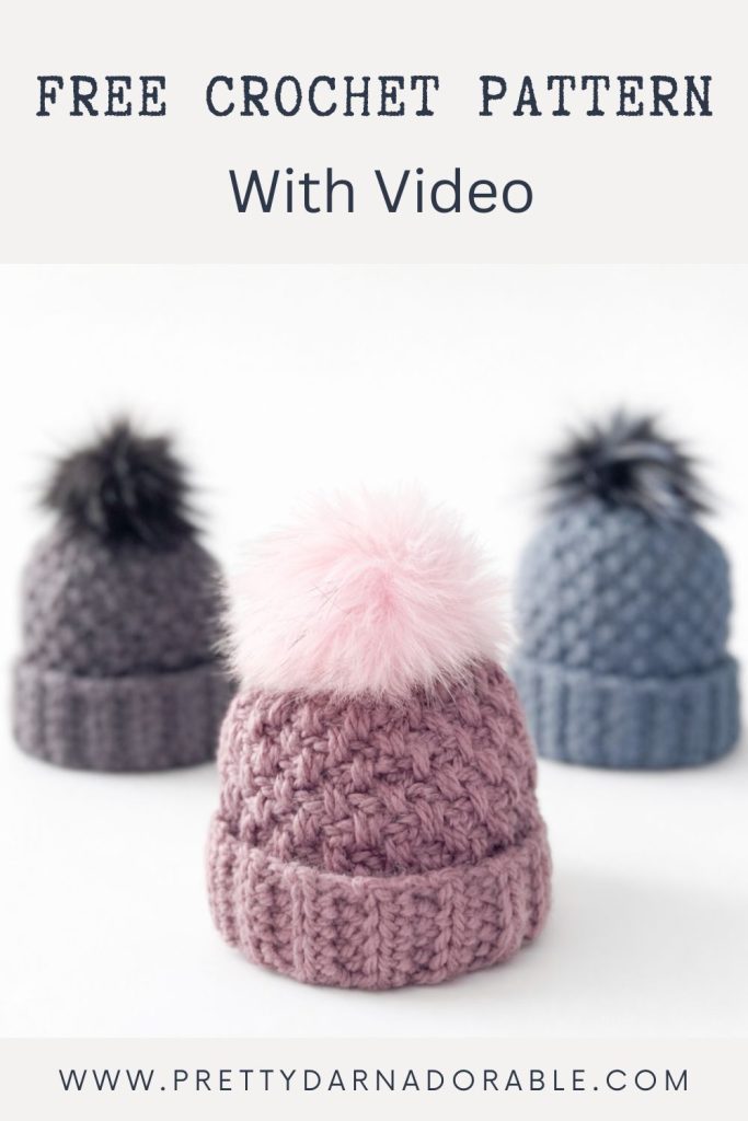 Three crocheted hats with fluffy pom-poms—pink, grey, and blue—are on a white surface. Text: Free crochet pattern with video. Free crochet pattern