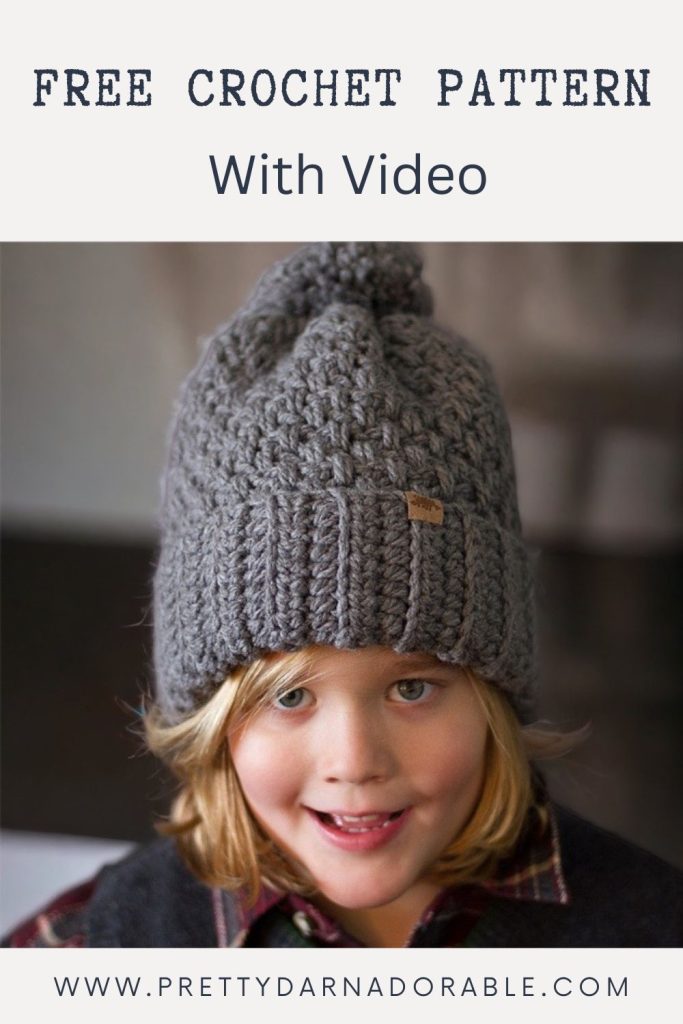 Child with long blonde hair wears a chunky gray crocheted beanie with pom-pom; text reads “Free Crochet Pattern With Video.” Website: www.prettydarnadorable.com. Free crochet pattern