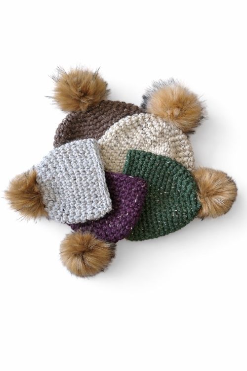 Five beanies with faux fur pom-poms in brown, cream, gray, purple, and green form a circle on a white background. Free crochet pattern