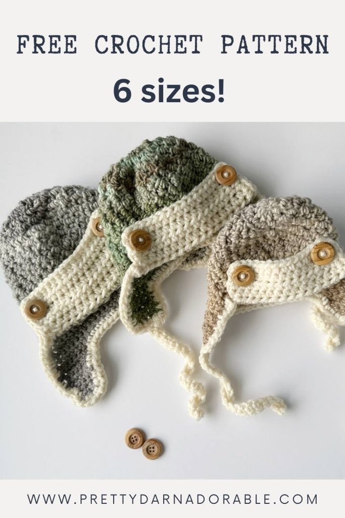 Three crocheted aviator hats in grey, green, and brown with cream trim and wooden buttons rest on a white surface with two spare buttons. Free crochet pattern