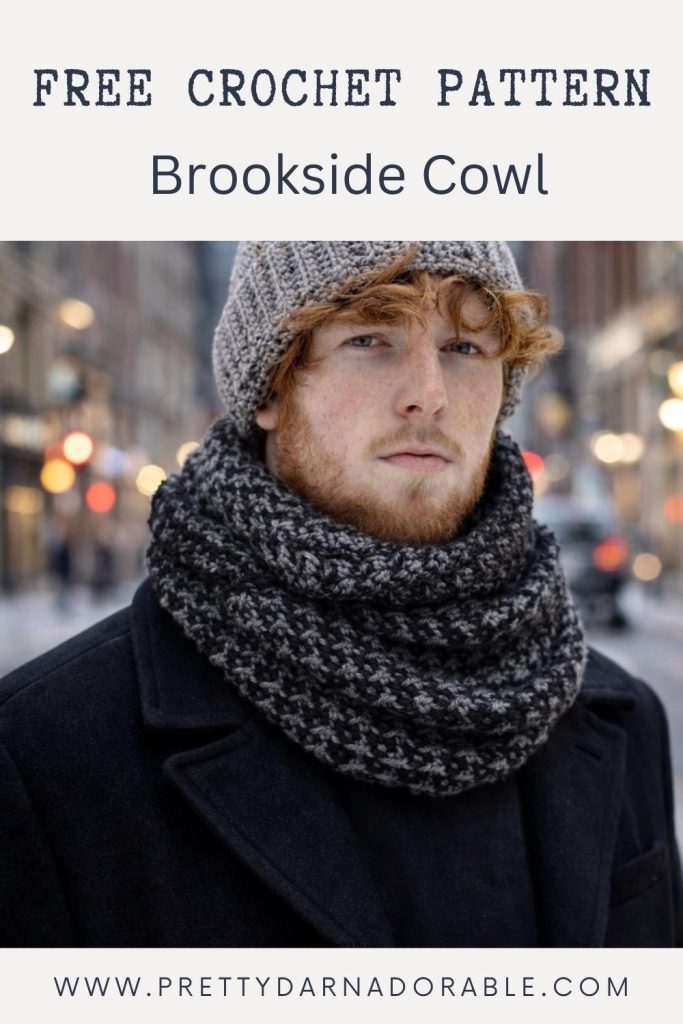 Man with curly red hair and beard in grey hat, chunky black and grey crochet cowl, dark coat; city street. Text: Free Crochet Pattern: Brookside Cowl. Free crochet pattern