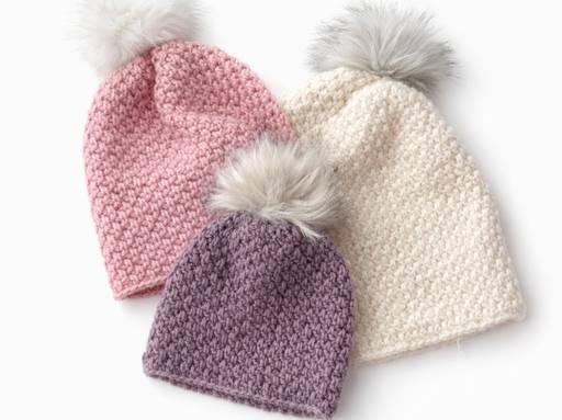 Three soft hats with fluffy pom-poms in pink, purple, and cream overlap on a white background; no visible text or promo info. Free crochet pattern