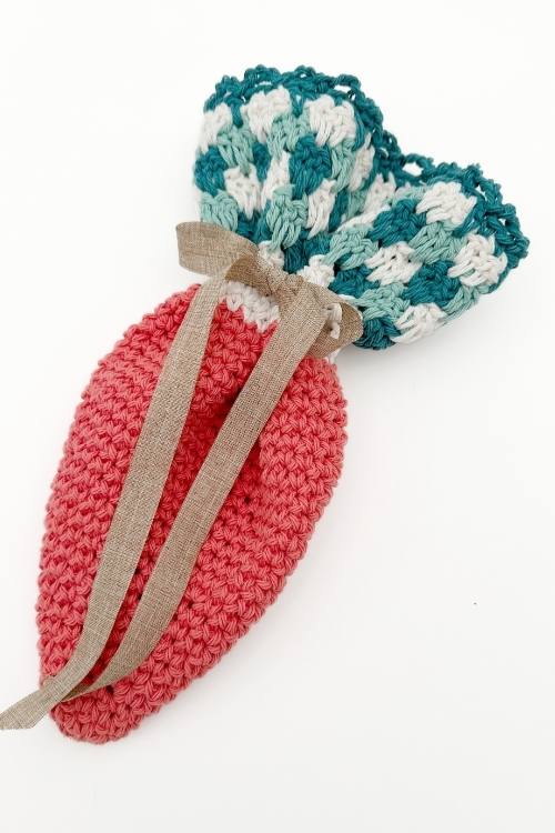 Crochetedcarrot treat bag with orange body, green-white top, beige ribbon on white background; highlights treat bag pattern. Free crochet pattern