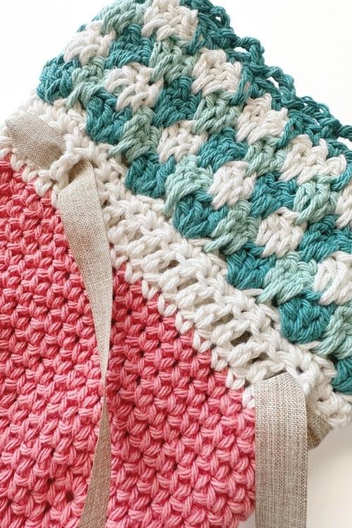 Close-up of a Crochet Carrot Treat Bag with pink, white, green, and teal stitches and beige ribbon woven through the white section. Free crochet pattern