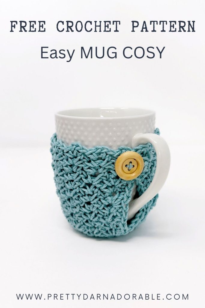 White mug with a textured blue crochet cosy and wooden button; text reads Free Crochet Mug Cozy Pattern, Easy Mug Cosy, www.prettydarnadorable.com. Free crochet pattern