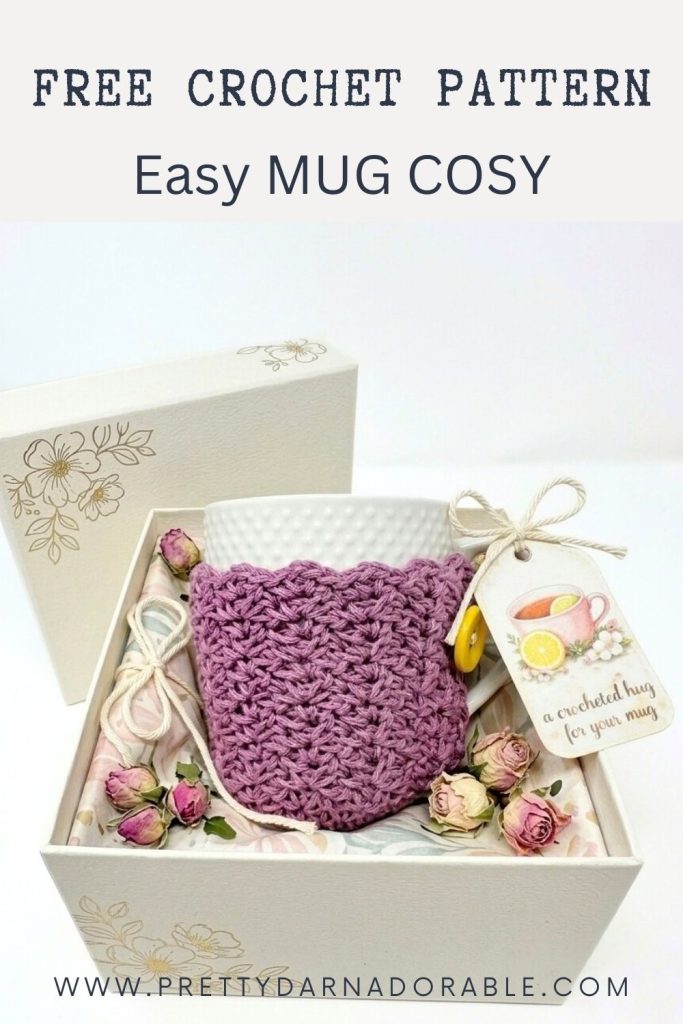 A gift box with a white mug in a purple crochet cozy, dried flowers, and tag; promo text: free mug cozy pattern at prettydarnadorable.com. Free crochet pattern
