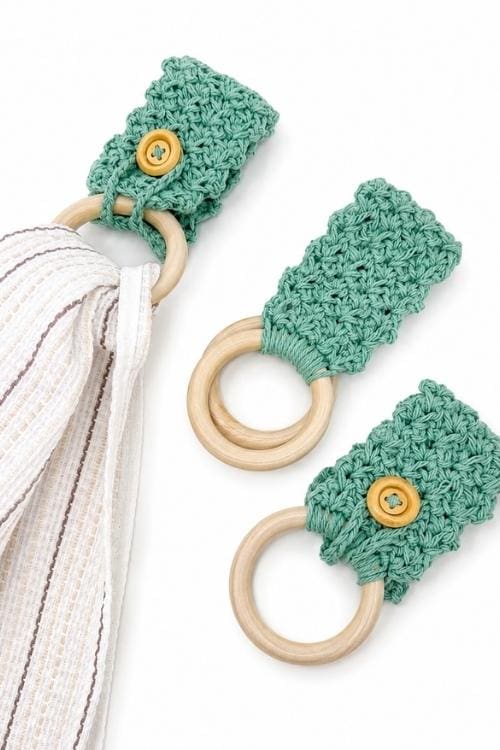 Two wooden rings with green crocheted holders and yellow buttons; one holds a folded white-beige striped fabric, one is empty. Free crochet pattern