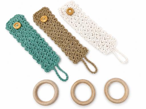 Three crocheted straps in green, tan, and white with button closures are placed above three wooden rings on a white background. Free crochet pattern