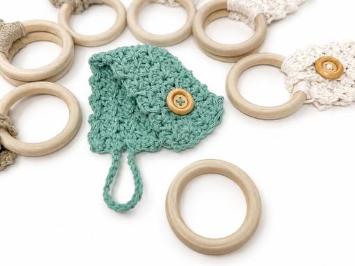 A green crocheted leaf with a button rests among wooden rings, some wrapped in neutral crochet bands, all on a white background. Free crochet pattern