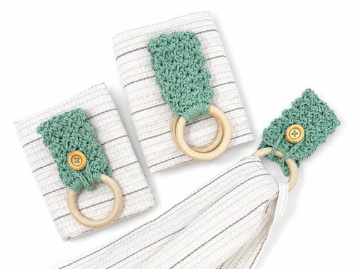 Three striped cloth napkins with green crocheted rings, wooden buttons, and rings are arranged on a neutral surface. Free crochet pattern