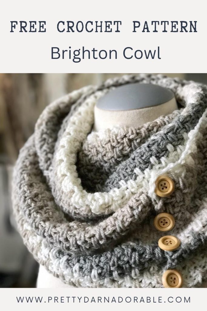 A mannequin wears a chunky, textured crochet cowl in neutral colors with wooden buttons. Text on the image says "Free Crochet Pattern Brighton Cowl" and "www.prettydarnadorable.com". Free crochet pattern