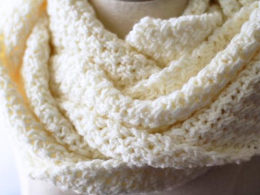 A close-up of a thick, white scarf with a soft, textured pattern is wrapped around a mannequin’s neck. No text or promotional info is visible in the image. Free crochet pattern