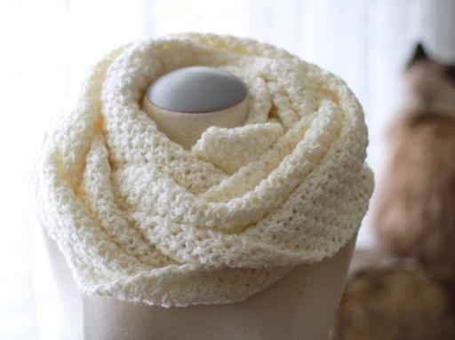 A cream-colored, thick-textured infinity scarf is wrapped around a dress form’s neck in soft, natural lighting. Free crochet pattern
