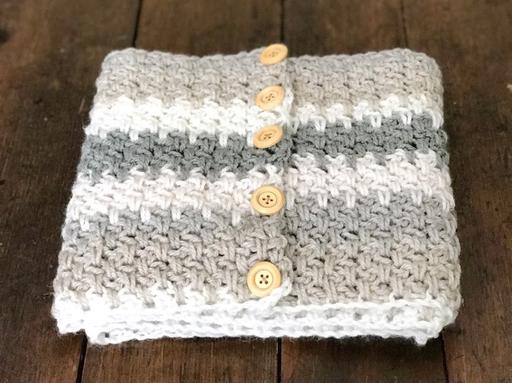 A folded, chunky blanket with gray and white stripes and five wooden buttons lies on a wooden surface. Free crochet pattern