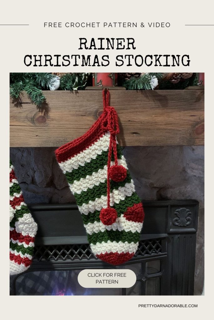 A crochet Christmas stocking with red, green, and white stripes hangs on a mantle decorated with greenery. Text above reads: “Free crochet pattern and video.”. Free crochet pattern