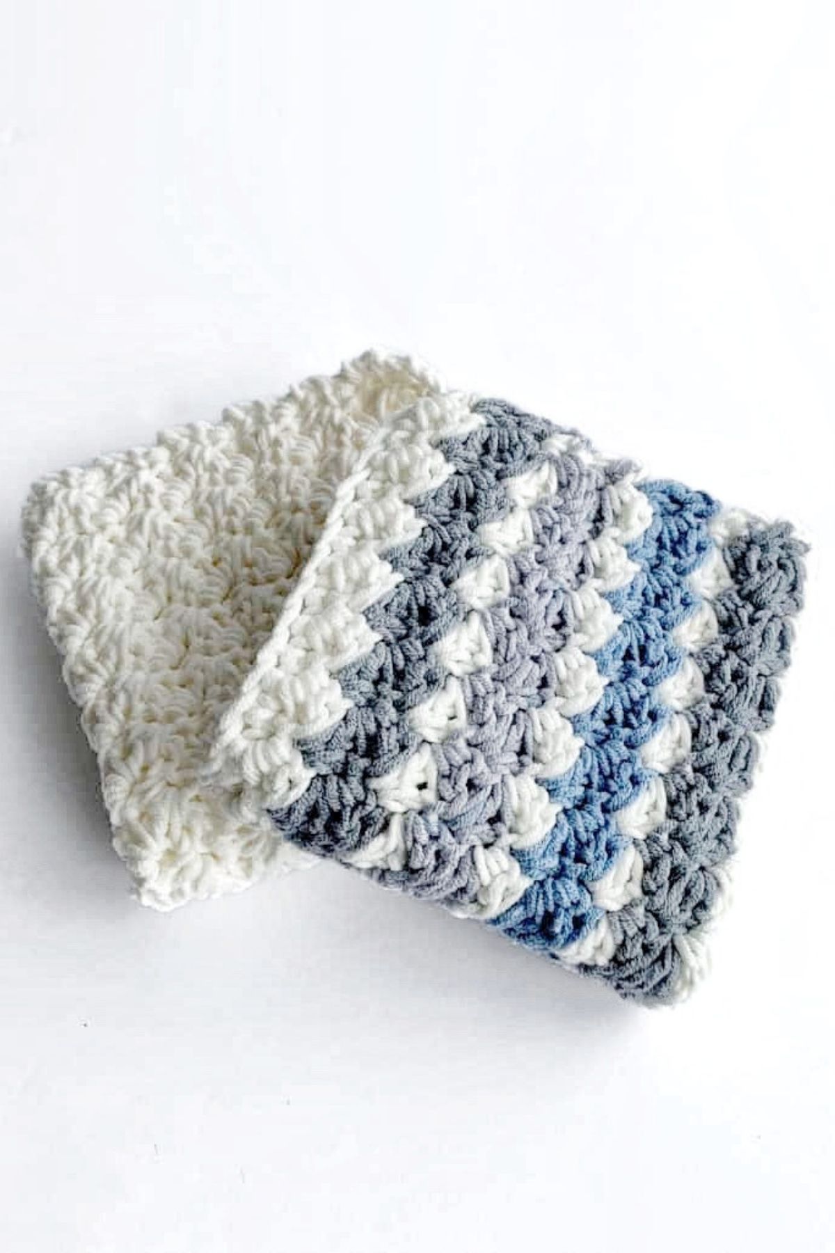 Two crocheted washcloths on a white background: one is solid white, the other striped in white, gray, and blue. Both have a textured, scalloped pattern and no visible text or promotional material. Free crochet pattern