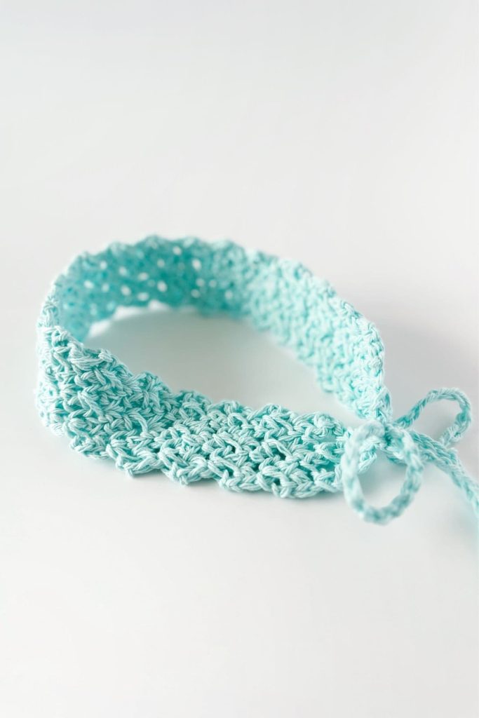 A light blue crocheted headband with a textured pattern and a tied bow is shown against a white background. No visible text or promotional elements appear in the image. Free crochet pattern
