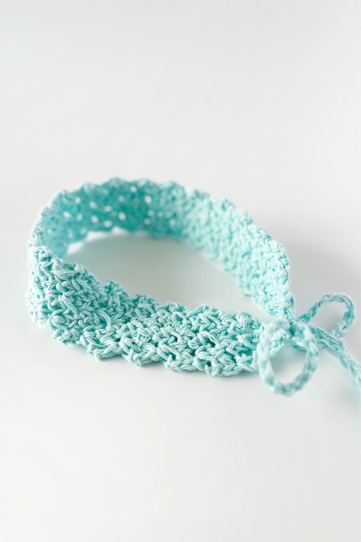 A light blue crocheted headband with a textured pattern and a tied bow is shown against a white background. No visible text or promotional elements appear in the image. Free crochet pattern