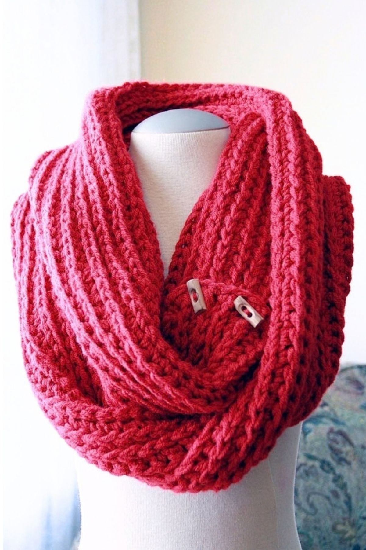 A red crochet knit look cowl with a ribbed, textured appearance and two light-colored wooden buttons, displayed on a mannequin. Free crochet pattern
